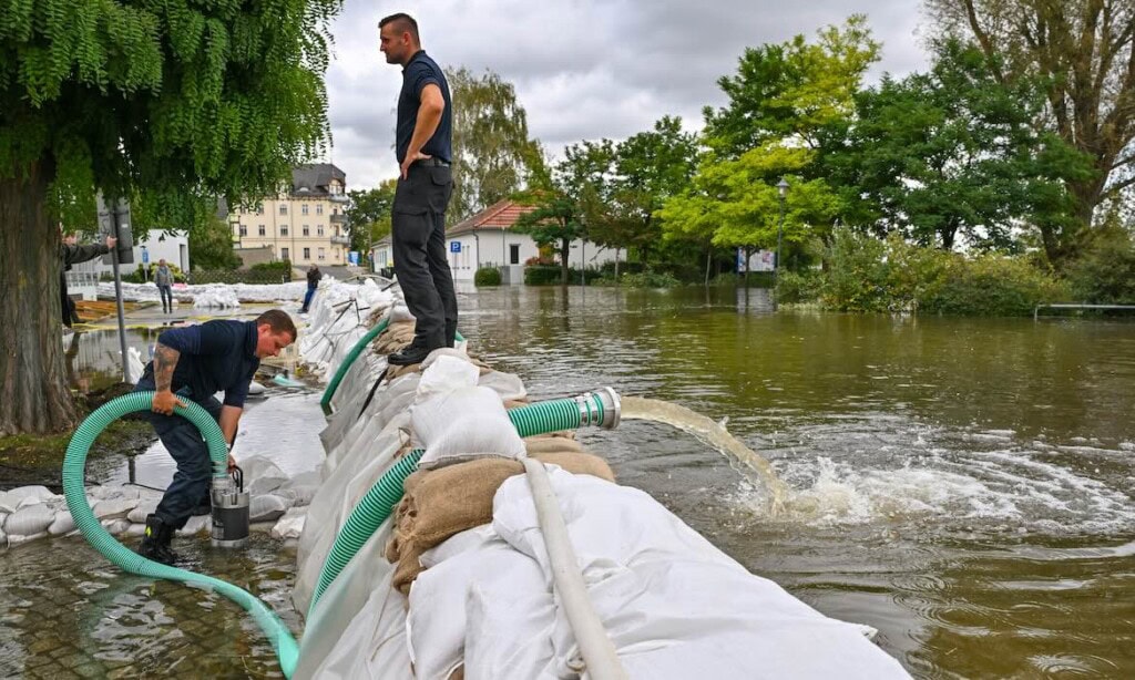 Menschen sichern vor Hochwasser mit Sandsäcken und Pumpen.