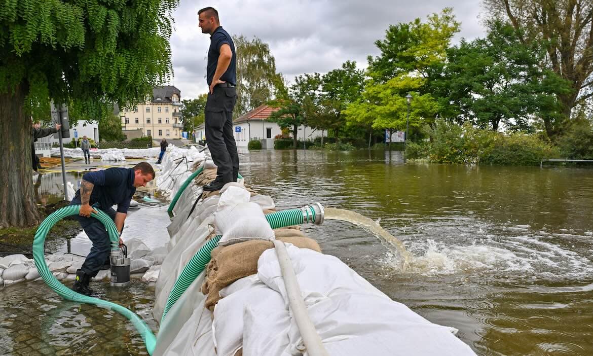 Menschen sichern vor Hochwasser mit Sandsäcken und Pumpen.