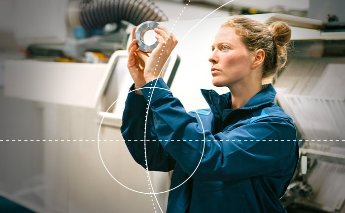 Frau überprüft ein technisches Bauteil in einer Werkstatt.