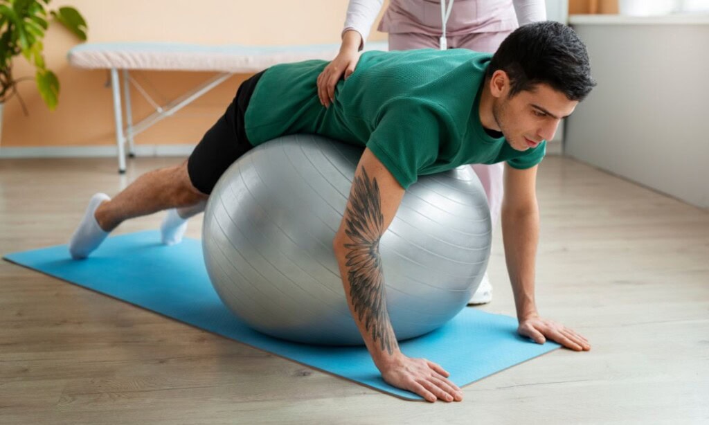 Mann trainiert mit Gymnastikball auf Yoga-Matte im Fitnessraum.