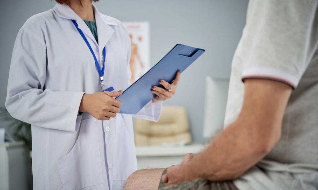 Ärztin mit Tablet im Gespräch mit Patient im Behandlungszimmer.