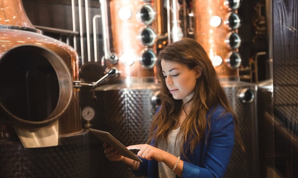 Frau in blauer Jacke liest in einer Brauerei auf einem Tablet.