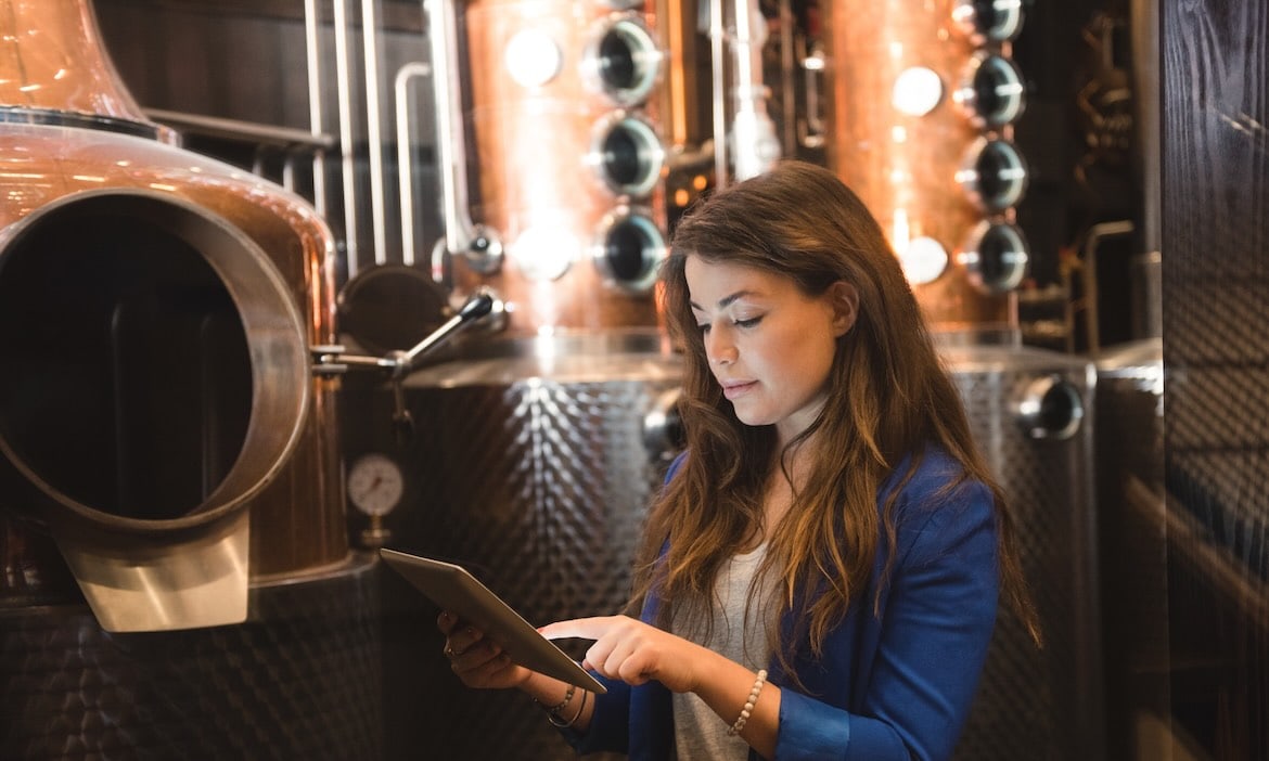 Frau in blauer Jacke liest in einer Brauerei auf einem Tablet.