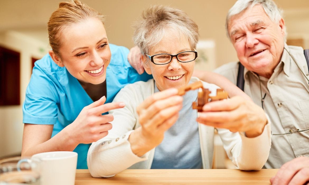 Pflegekraft unterstützt ältere Dame beim Spielen eines Brettspiels.