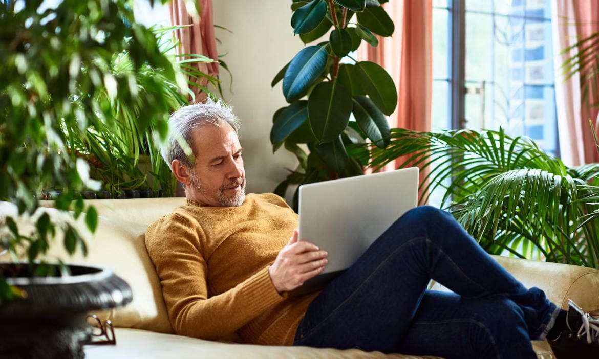 Mann entspannt auf Sofa liest auf Laptop in Wohnzimmer.