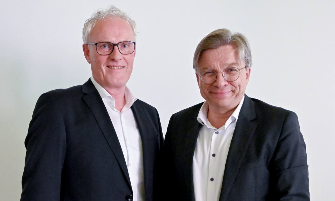 Zwei Männer in Anzügen bei offizieller Fusion.