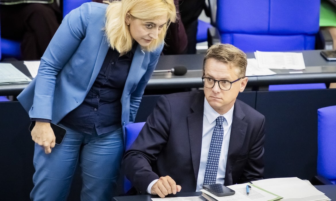 Zwei Politiker im Gespräch im Parlament, einer sitzt, die andere steht.