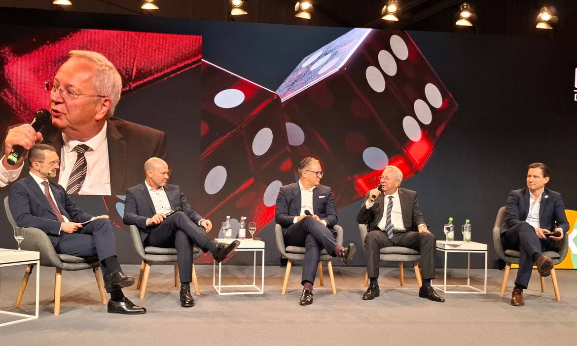 Paneldiskussion bei Messe mit mehreren Sprechern auf Bühne.
