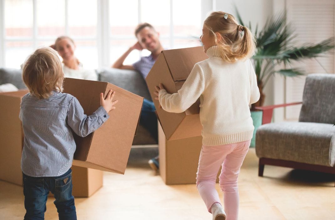 Kinder tragen Umzugskartons in hellem, modernem Wohnzimmer.