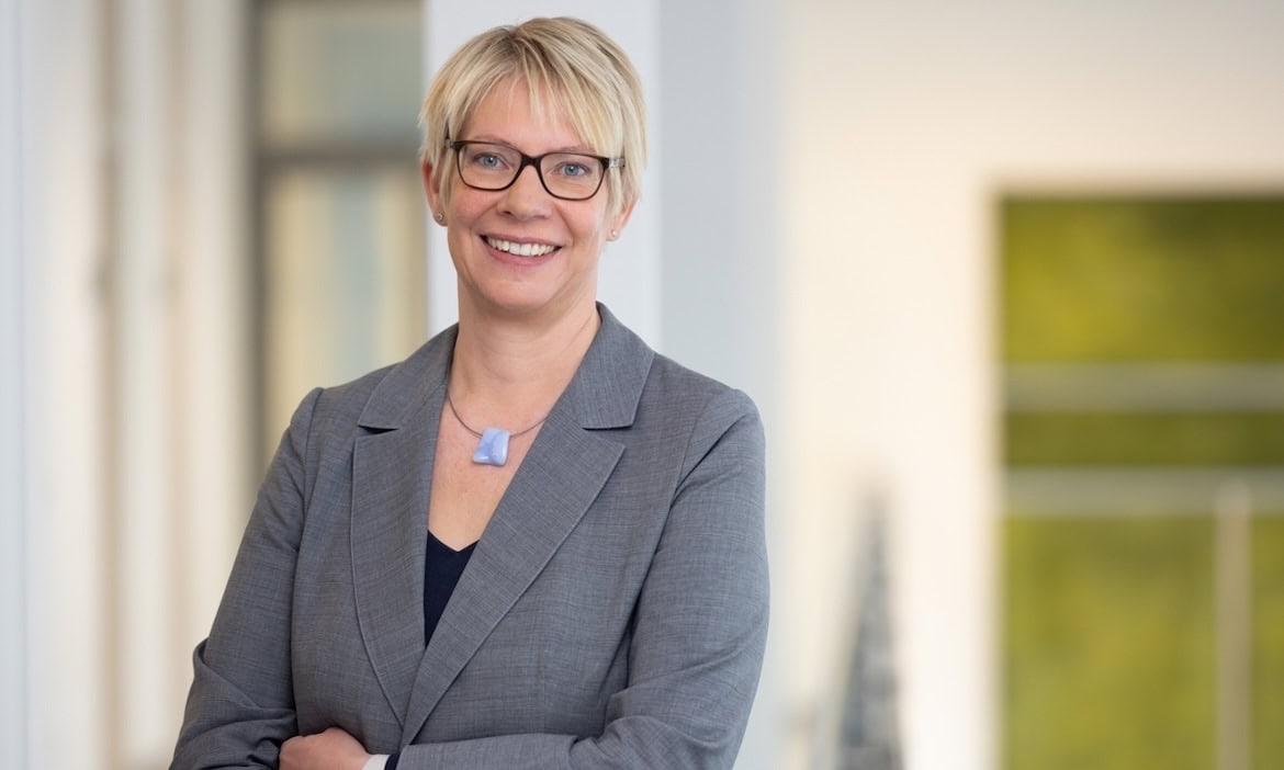 Selbstbewusste Geschäftsfrau mit Brille und grauem Blazer.