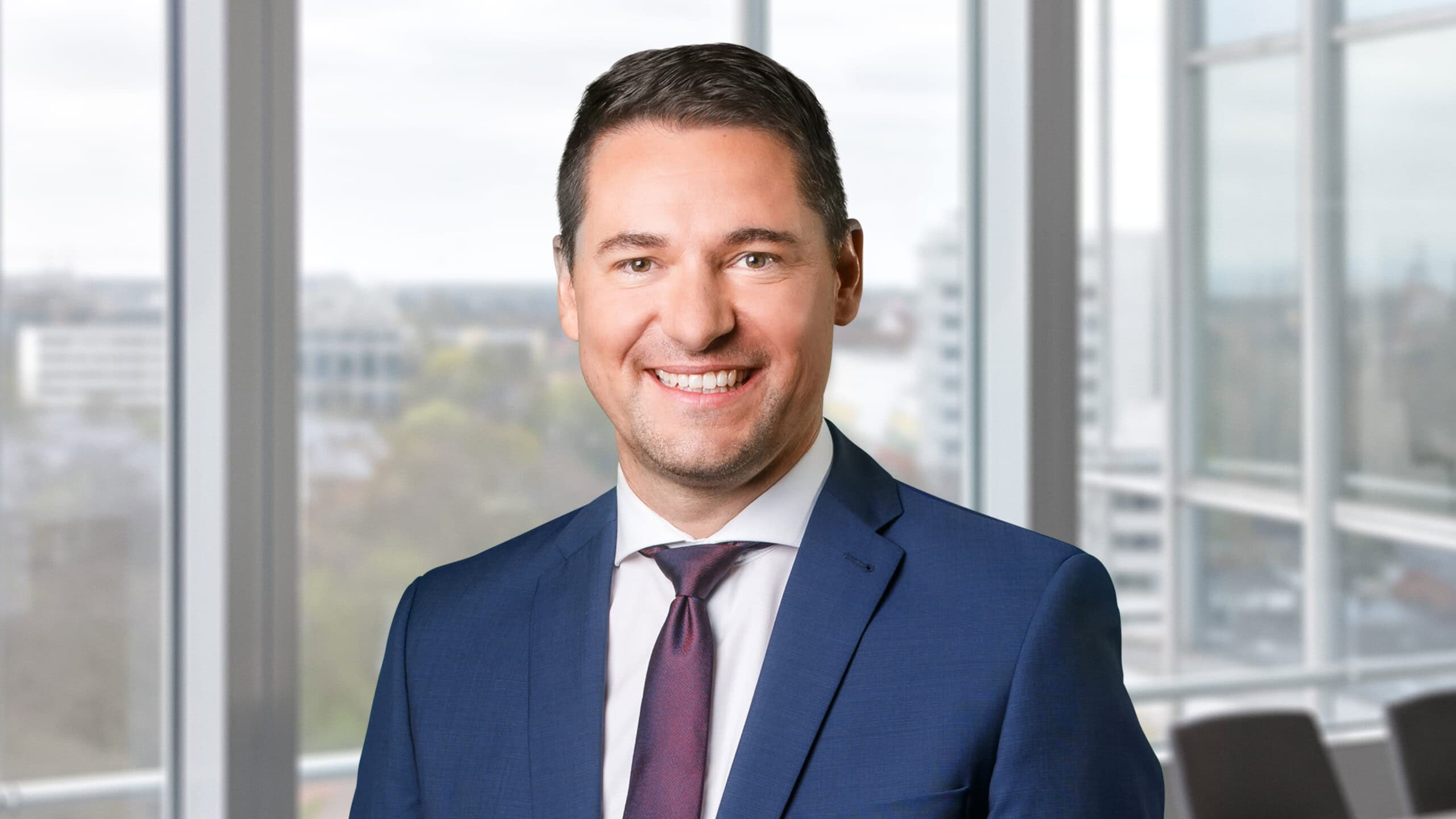 Geschäftsmann in Anzug vor Fenster mit Stadtblick.